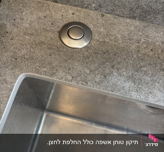 כיור נירוסטה עם כפתור מתכת על משטח אבן